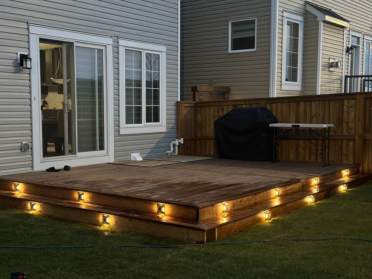 Multi-level wooden deck with integrated LED lighting and privacy fence at dusk